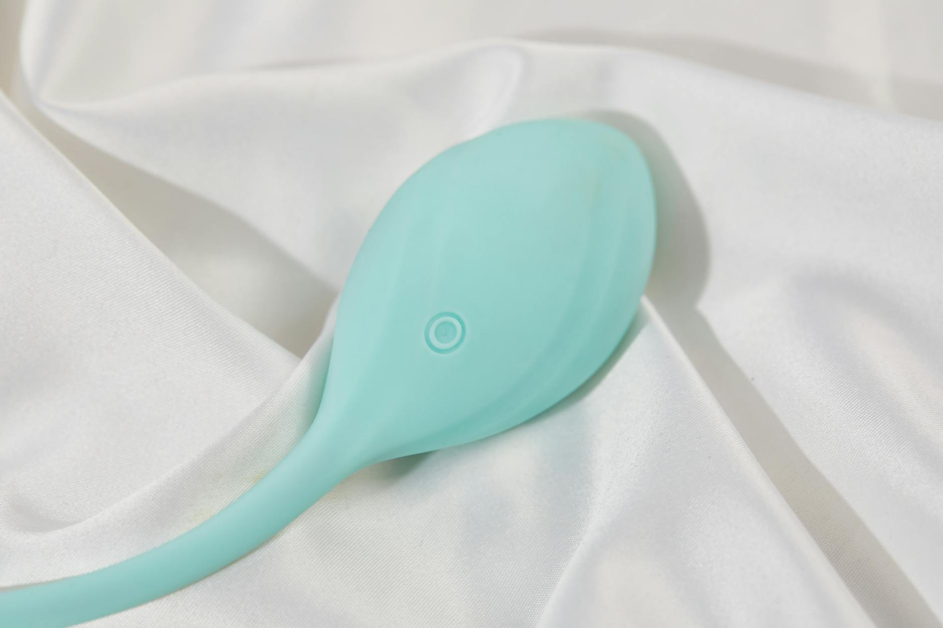 A teal clitoral vibrator resting on soft white silk