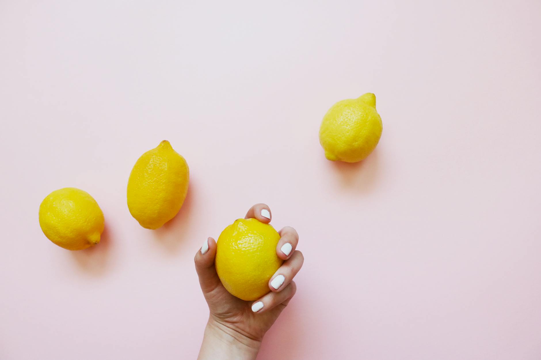 A hand holding a fresh lemon on soft pink background, symbolizing renewed intimacy and pleasure