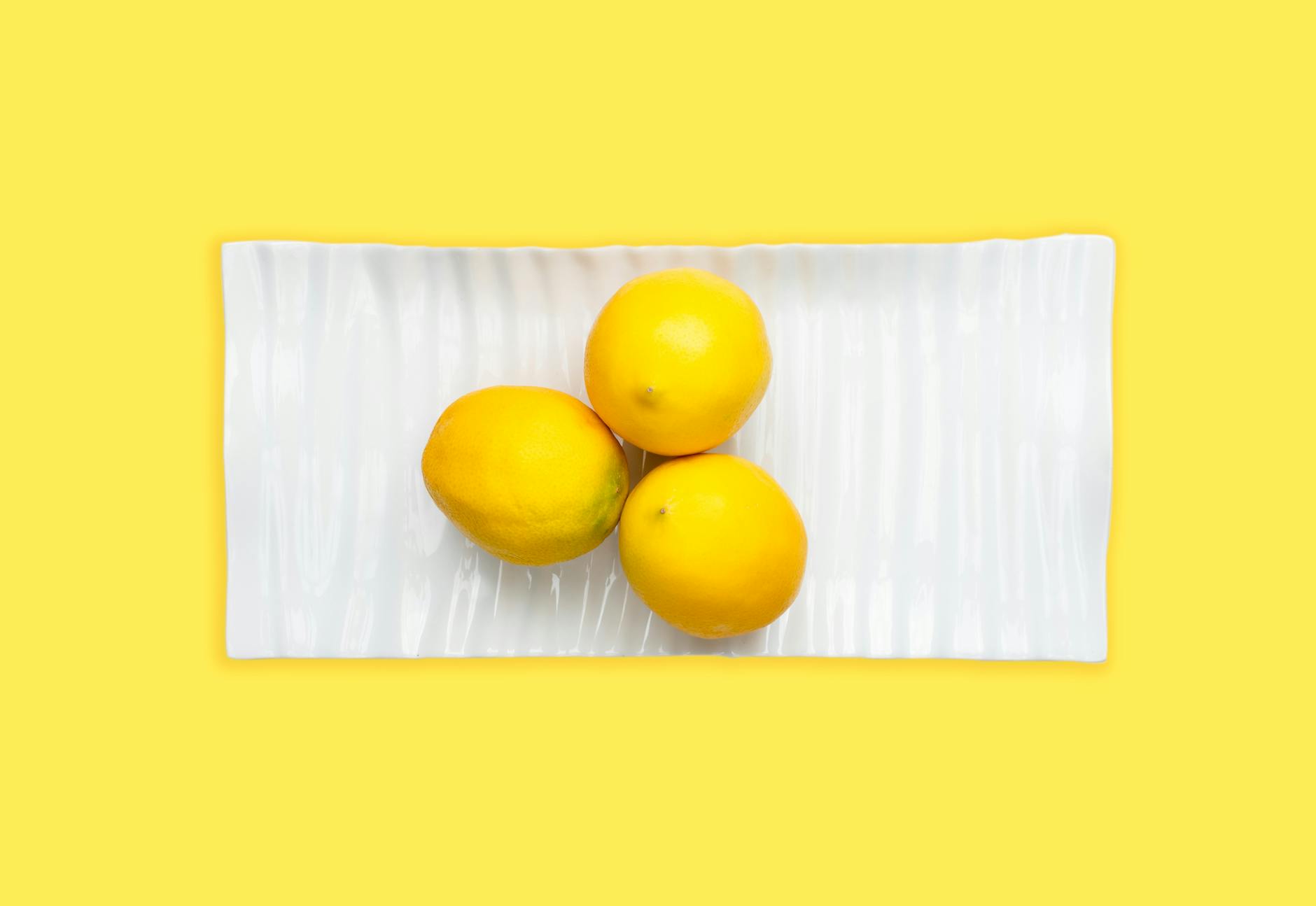 Hand holding a fresh lemon on a soft pink background surrounded by additional lemons, symbolizing fresh approaches to pleasure after age 50