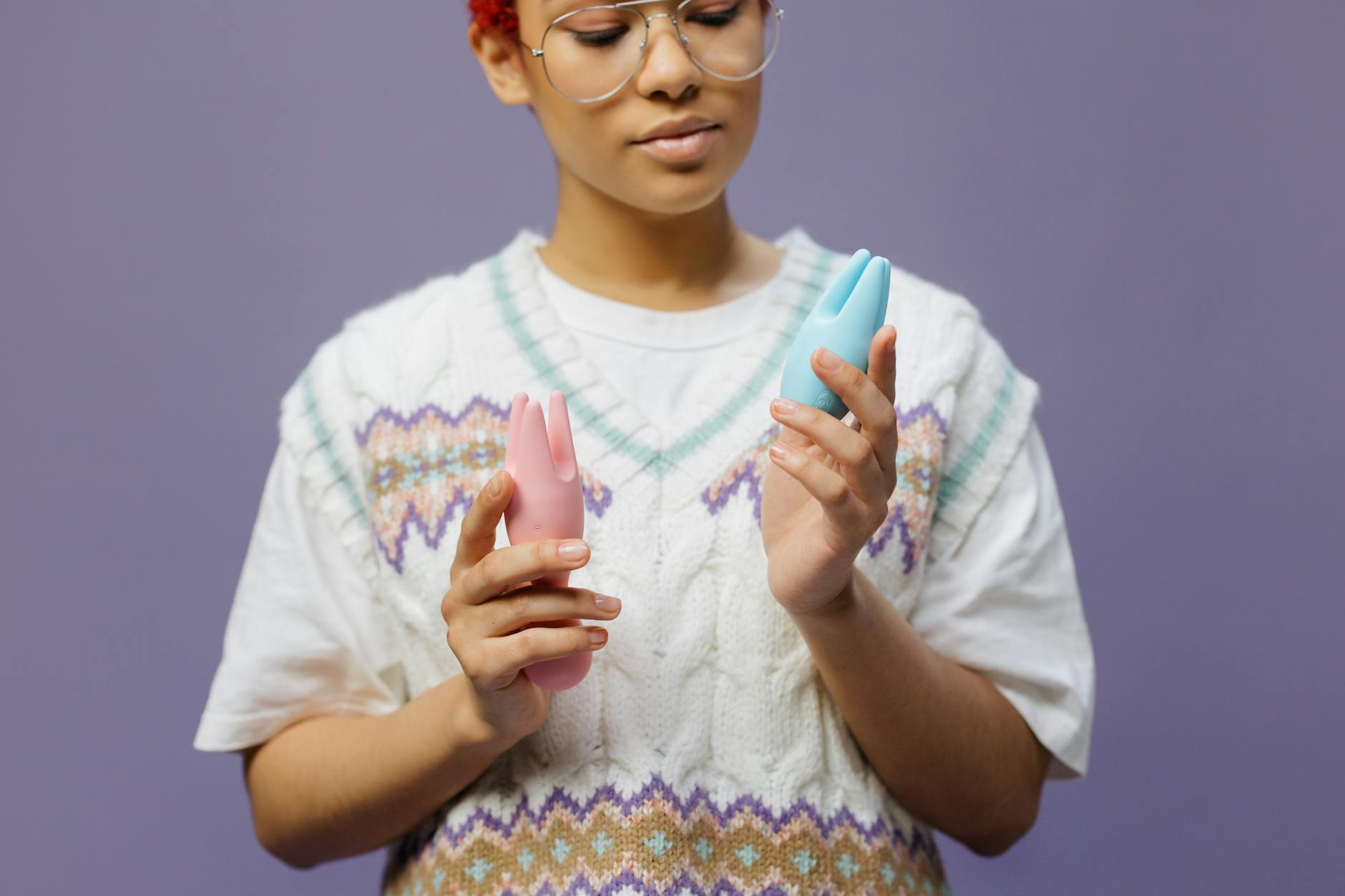 Woman holding pink and blue silicone clitoral vibrators in contemplative pose