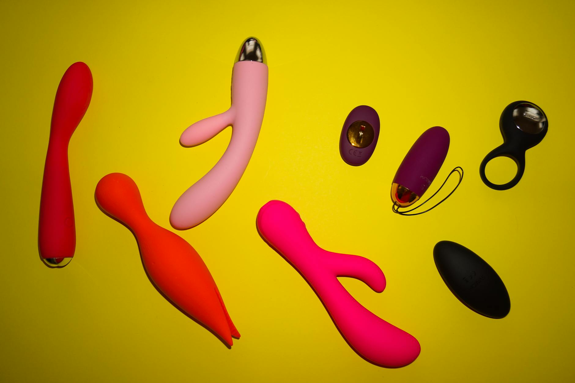 Vibrant collection of colorful clitoral vibrators and massagers arranged on a bright yellow background