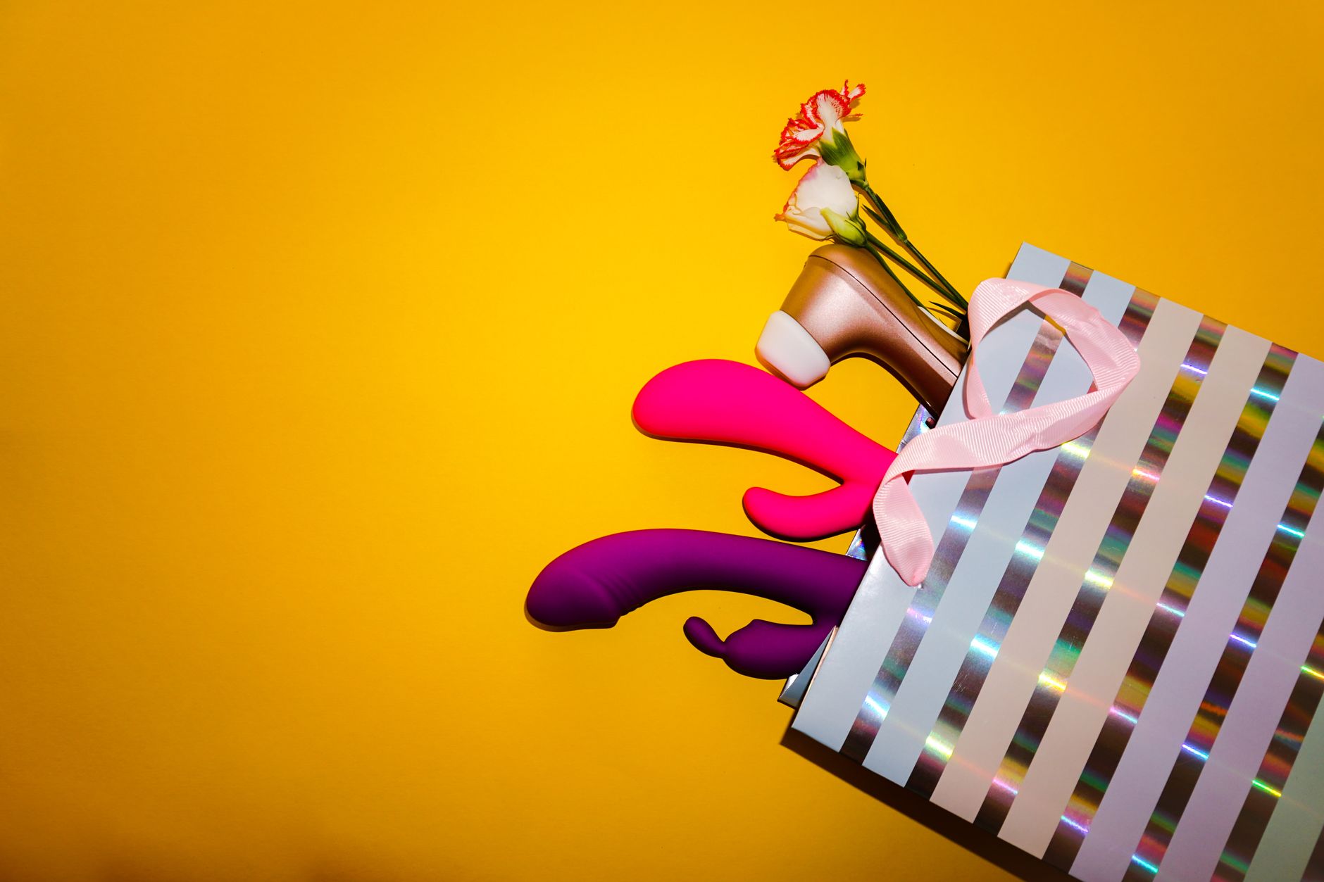 Colorful vibrators with flowers in a holistic gift bag, set against a bold yellow background.